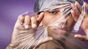 Nonbinary androgynous Twink peeping through a hole of foil. 