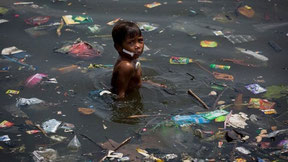 poor boy standing between large amounts garbage polluting river