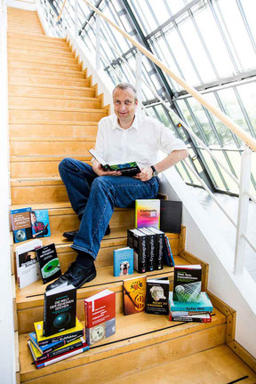 Der Author sitzt auf einer Treppe, umrahmt von seinen Büchern.