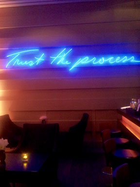 Raum mit blauer Neon-Schrift an der Wand: Trust the process. An den Coachingprozess glauben. Vertrauen in den Coachingprozess entwickeln.
