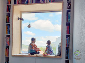 Modernes Holzhaus in Goßheim mit in die Wandnische eingelassene Sitzfenster mit Panorama Ausblick, Nischenfenster mit Fichtenrahmen, Bücherregal und Stauraum in weiß und Sitzgelegenheit, Sitzplatz am Fenster mit Stauraum u. Bücherregal