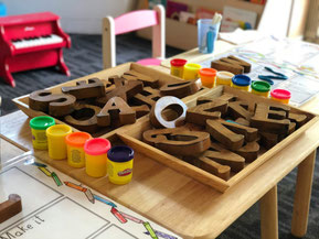 Auf einem Tisch sind Malfarben und ein Holzalphabet zu sehen.