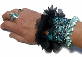 photo d'un bracelet manchette original de créateur noir et bleu turquoise à volant de pétales en tulle et froufrous porté sur le poignet