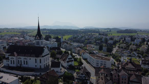 Luftaufnahme mit Kirche von der Seite her gesehen am linken Rand; Wohnhäuser am rechten Rand; im Seetal