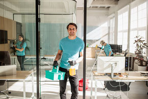 Mitarbeiter von Km Gebäudeservice Lübeck reinigen gründlich Büroräume und Glasflächen in einem Gebäude in Schleswig-Holstein, während im Hintergrund weitere Reinigungskräfte Fenster und Arbeitsbereiche pflegen.