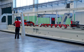 Foto von einer speziell angefertigten Maschine, die mindestens 6 Meter lang ist, vor ihr steht eine Person in rotem T-shirt und schwarzer Hose.