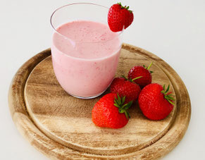 Smoothie im Glas auf Holzbrett mit fünf Erdbeeren Erdbeersmoothie mit Joghurt