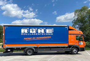 Ein orangener Lkw mit blauer Plane mit einem weissen Schriftzug der Firma Rühe Rolladentechnik. Ein weiterer Schriftzug ist ornage und heißt Partner des Fachhandwerks.