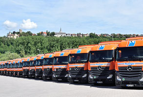 Man sieht ordentlich nebeneinander geparte Lkw in einer langen Reihe. Im Hintergrund  ist die Burg Krautheim zu sehen. Der Himmel ist blau mit weissen Wolken.