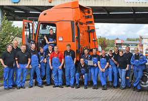 Die Werkstatt-Crew hat sich vor dem Truck aufgestellt. Etwa 18 Mitarbeiter haben blaue und zum Teil schwarze Kleidung an.