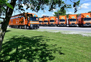 Viele orangene Lkw der Rüdinger Spedition stehen in einer Reihe nebeneinander. Vor ihnen steht vorne links ein weiterer Lkw.