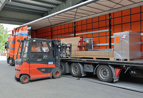 Ein Lkw ist an der Seite komplett geöffnet. Die Plane ist zusammengeschoben. Ein Stapler auf der linken Bildseite hebt ein Langgutstück auf die Ladefläche.