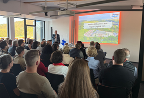 Ein Blick in das Großraumbüro. Einer Besuchergruppe, ganz vorne im Bild, wird an einem Arbeitsplatz der Arbeitsablauf erklärt.