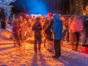 Viele Menschen in bunt beleuchteter Waldschneiße bei einer Weihnachtsfeier