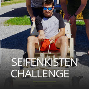 Mann mit Sonnenbrille sitzt in einer Seifenkiste, Schriftzug: SEIFENKISTEN CHALLENGE
