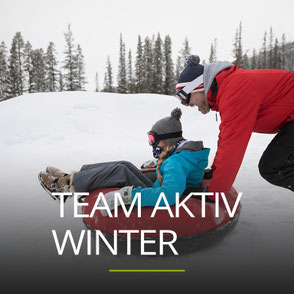Ein Mann schiebt eine Frau im Snowtube, Schriftzug: TEAM AKTIV WINTER