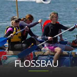 Eine Gruppe paddelt auf einem selbst gebauten Floß, Schriftzug: FLOSSBAU