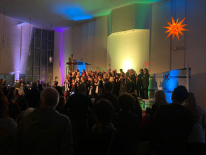 Blick von rechts aus dem Publikum auf der Bühne: UGc & Joyful Singers auf der Bühne, links daneben die Band, rechts oben ein gelber Herrnhuter Stern