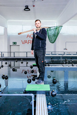 Mitarbeiter in einer Fischzucht steht mit Kescher vor einem Wasserbecken – authentische Unternehmensreportage mit Fokus auf Produktionsprozesse.