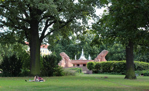 Menschen liegen auf dem Rasen unter Bäumen. Arnswalder Platz mit Stierbrunnen: Foto: Helga Karl