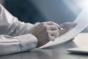 Eine Hand mit einem Stift und Papier am Schreibtisch.