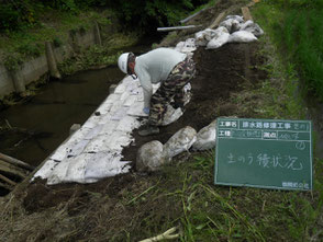 崩落した部分に、盛土をして最後に土嚢を取付作業を完了している写真