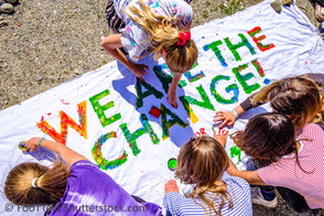 Jugendliche malen Transpartent, darauf steht "we are the change" Hoffnung für bessere Zukunft und Klimaschutz