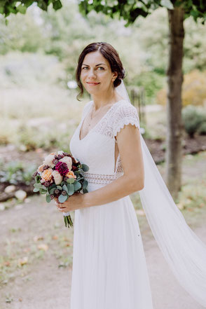 Halbportrait einer Braut, die seitlich zum Betrachter steht, ihren Brautstrauß hält und in die Kamera lächelt