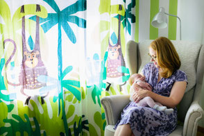 Mutter sitzt im Sessel im Kinderzimmer und hält liebevoll ihr schlafendes Neugeborenes im Arm.