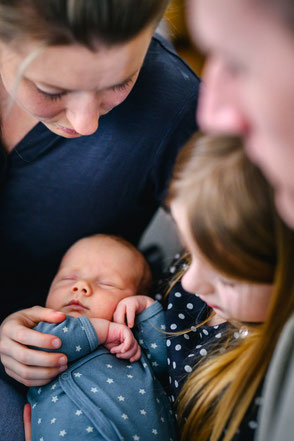Blick von oben auf schlafendes Baby im Arm der Schwester, Eltern genießen den Moment.