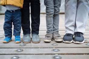 Junge Familie steht nebeneinander auf einer Holzbrücke, Fokus auf ihre Schuhe und Beine.