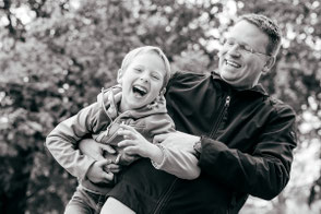 Vater spielt mit seinem Sohn, hebt ihn im Arm hoch und beide lachen.