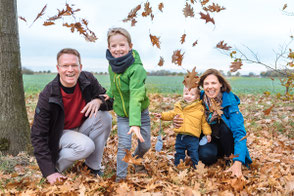 Glückliche Familie wirft lachend herbstliches Laub in die Kamera.