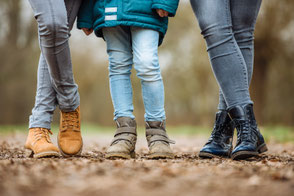 Drei Kinder stehen im Park lässig nebeneinander, Fokus auf ihre Schuhe.