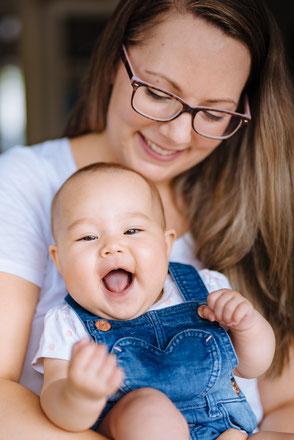 Mutter genießt einen fröhlichen Moment mit ihrem lachenden Baby auf dem Arm.