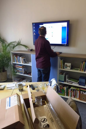 Ein Techniker bringt einen Fernseher an der Wand an im Büro von Ina Bärschneider