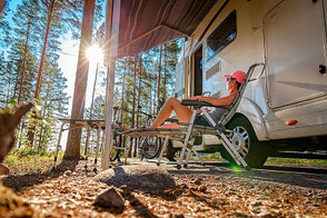 Frau sitzt vor Camper im Caravaning-Urlaub, gut versichert mit der ERGO Camping-Reiserücktritts-Versicherung