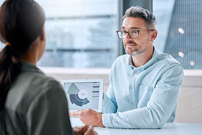 Finanmakler berät eine Kundin und zeig ein Chart am Laptop