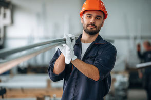 Ein Arbeiter mit orangem Helm trägt Aluminiumprofile