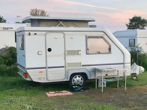 Ein kleiner Wohnwagen mit einem Hubdach steht auf einem Campingplatz