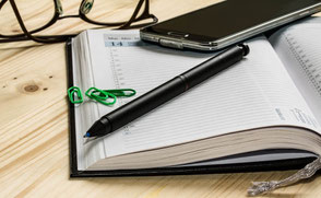 Notizheft, Block, Stift, Brille und Handy als tpisches Equipment.