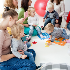 Mütter mit ihren Kleinkindern, die gemeinsam auf dem Boden sitzen und spielen.