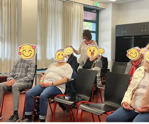 Die Teilnehmer einer Heilsession sitzen und Ina Paulus steht hinter 2 Teilnehmern und legt jedem eine Hand auf den Kopf