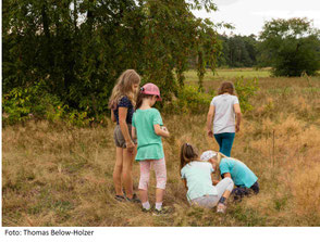 eine Gruppe Kinder beim Spielen auf Feld und Wiese, im Hintergrund Bäume