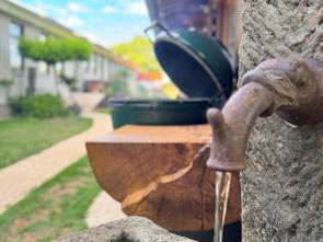 Historischer Natursteinbrunnen vor einer Grillstation aus massiver Geisinger Esche mit Big Green Egg im Gartenbereich