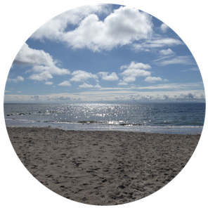 Wolken am hellblauen Himmel darunter das Meer und der Strand