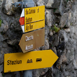 Wegweiser in Disentis, Surselva, Graubünden, zeigen die Richtung zum Kloster und zum Museium, zum Bahnhof (Staziun), nach Sedrun und Santa Catarina. Foto: Stefan Schwenke