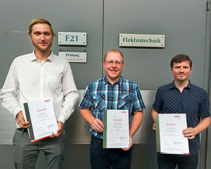 Drei Absolventen halten ihre Zeugnisse nach bestandener Lehrabschlussprüfung in der Hand
