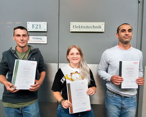 Drei Teilnehmer:innen der Ausbildung Elektrotechnik zeigen stolz ihre Abschlusszeugnisse