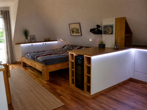 Einbauschrank nach Maß unter der Dachschräge mit integrierter Beleuchtung, Bettbereich und weiß-holzfarbener Möbellösung von Holzdesign Rapp